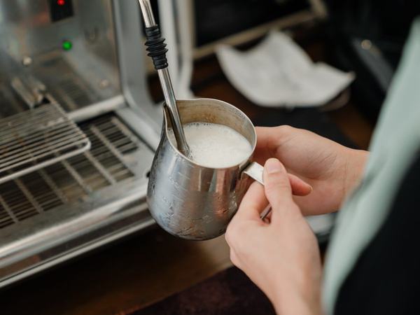 Steaming milk in a stainless pitcher at the espresso machine